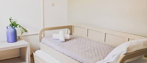 A single bed with a quilted mattress, a bedside table with a vase, and a wall-mounted TV.