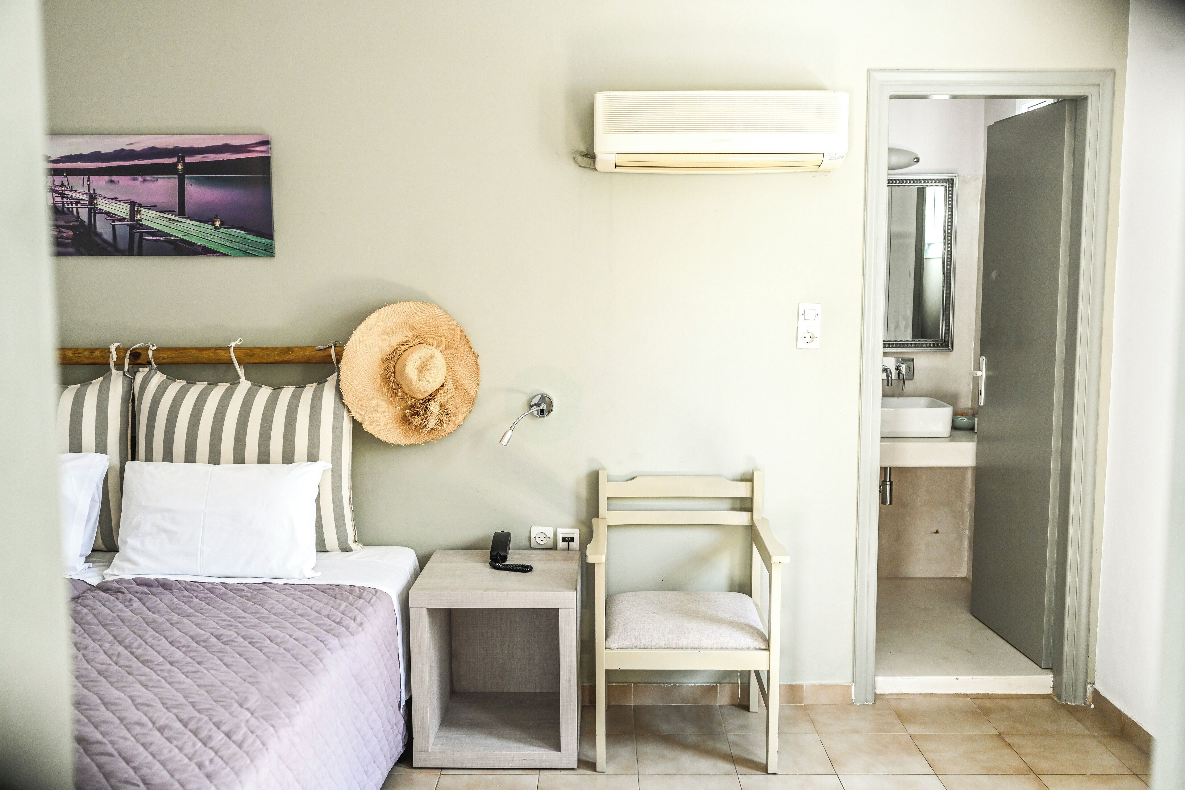A bedroom with a bed, bedside table, chair, and a wall-mounted air conditioner.
