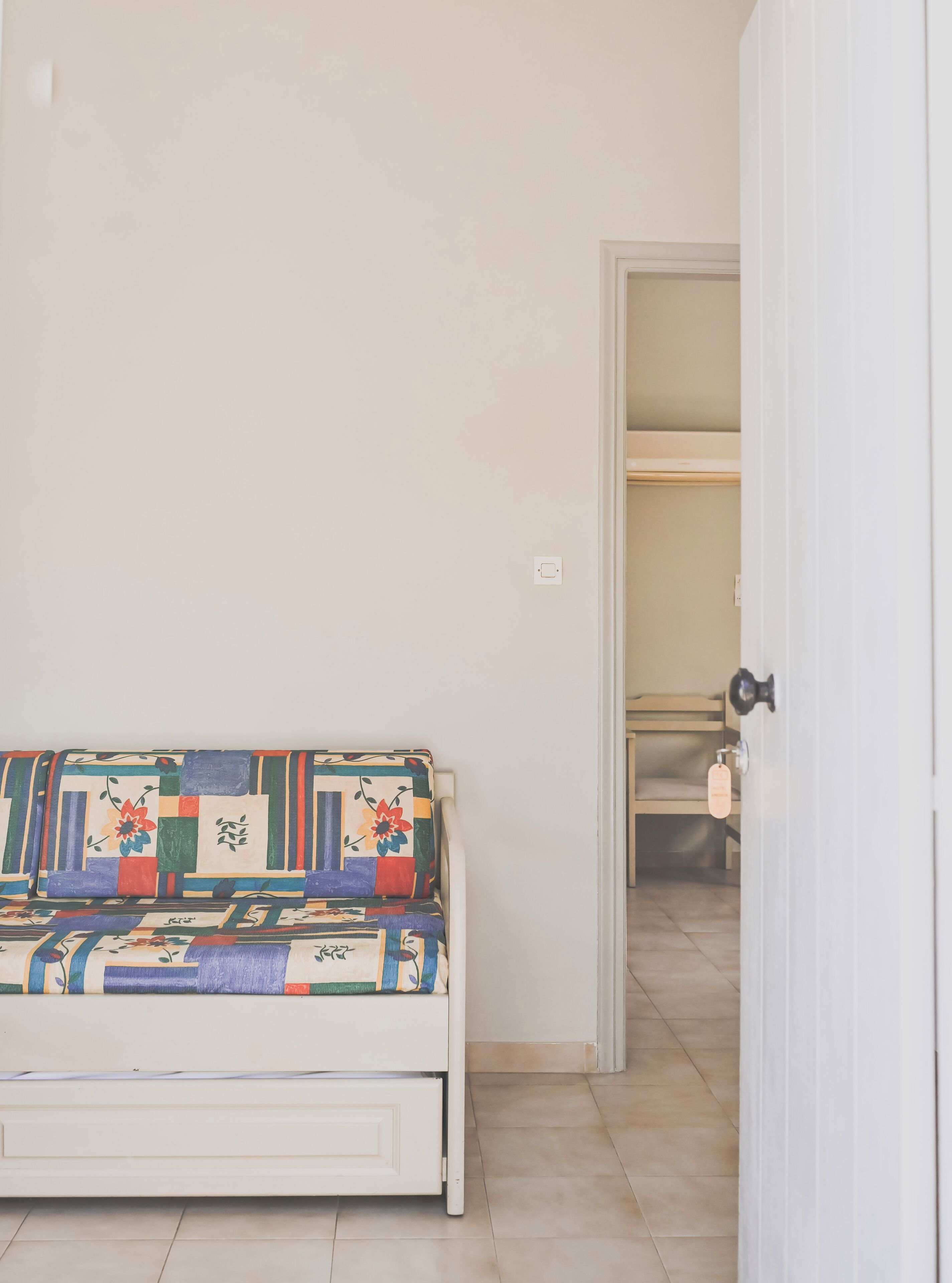 Un sofá blanco con un colcha colorida, una puerta blanca y un piso de baldosas.