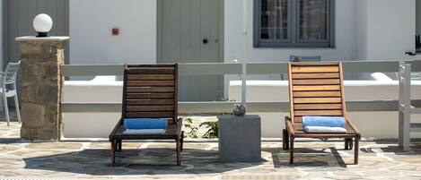Un espace aménagé au bord de la piscine, comprenant deux chaises longues en bois, un parasol blanc et un pilier en pierre.