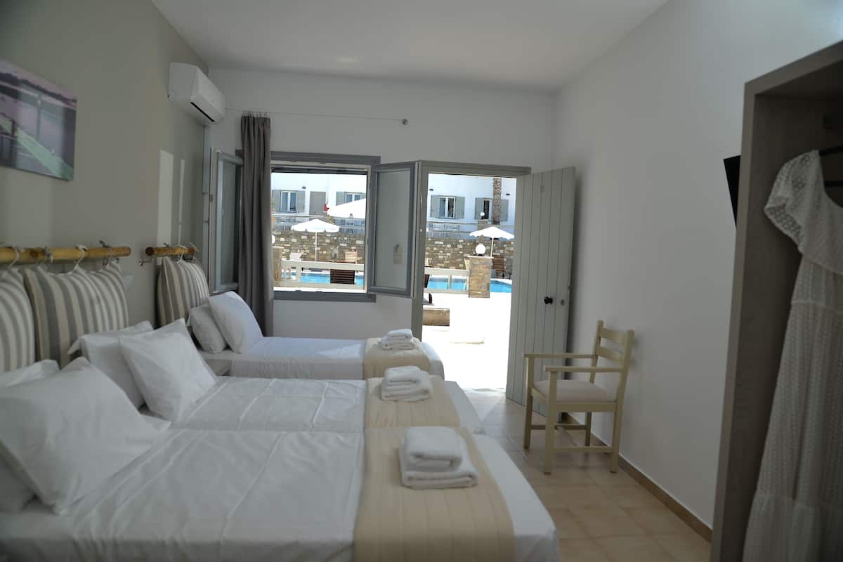 Habitación de hotel con dos camas, una silla y vistas a la piscina y edificios.