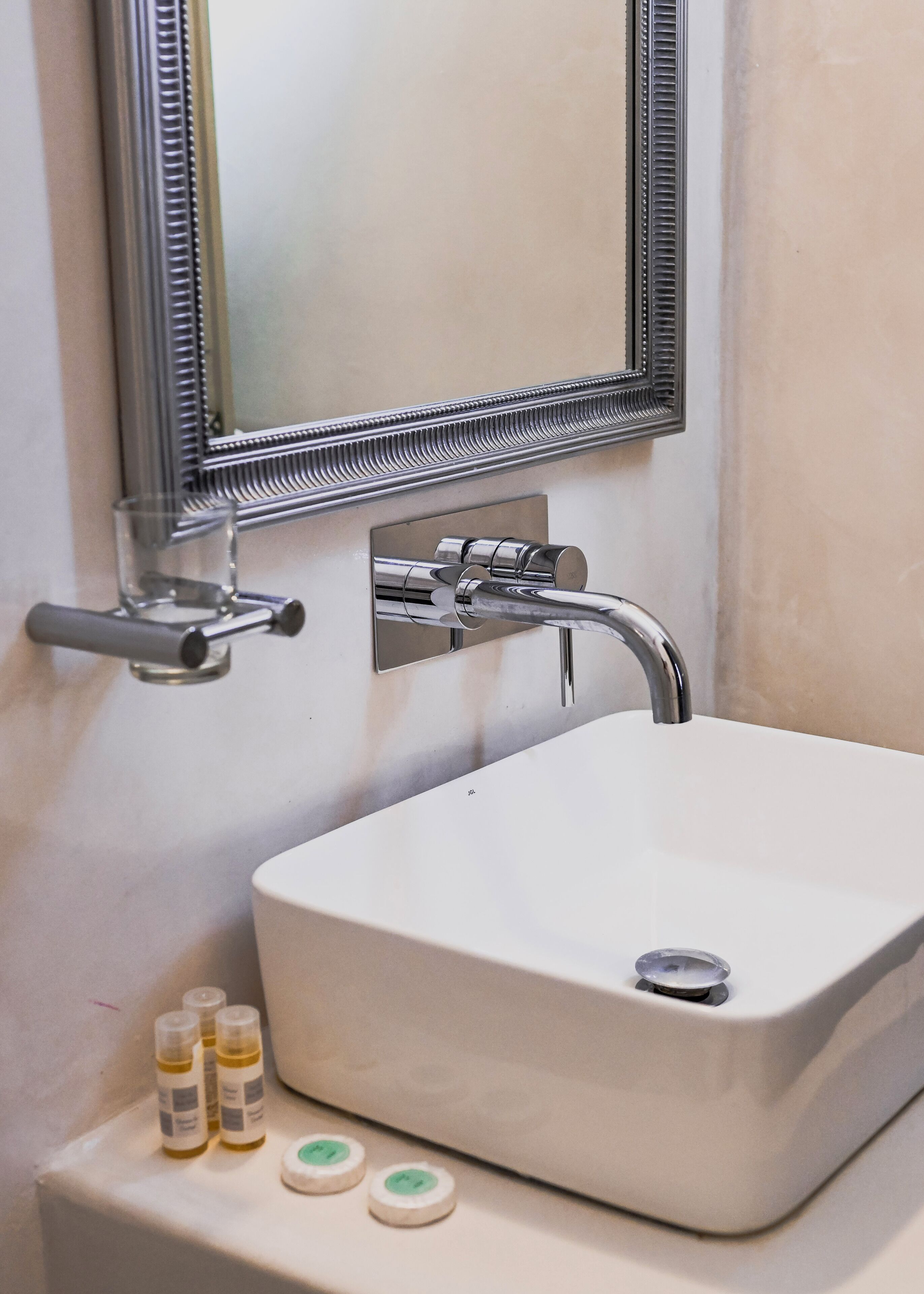 A bathroom sink with a mirror, faucet, and three small bottles on the counter.