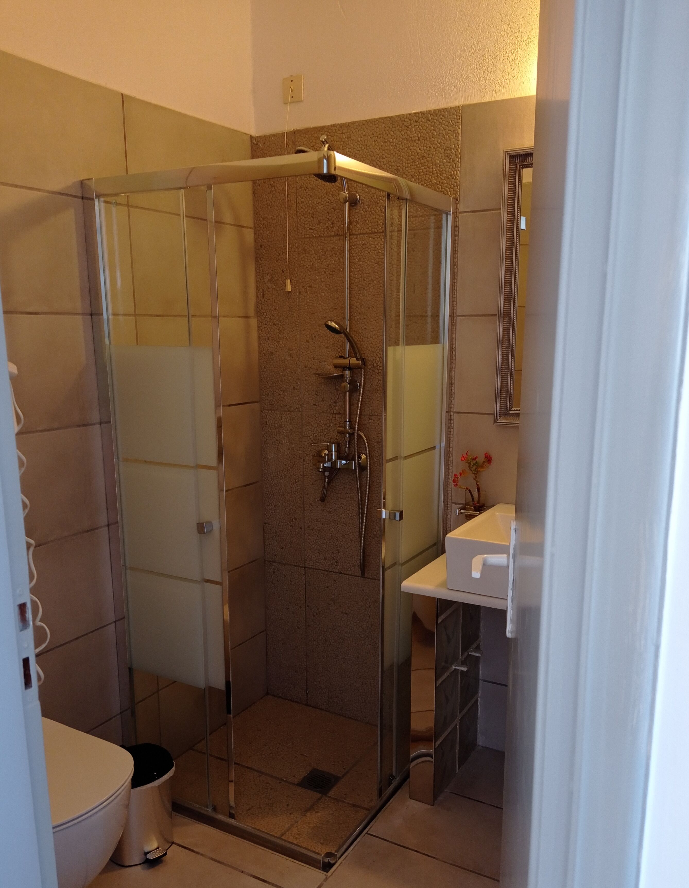 A glass-enclosed shower stall with a handheld showerhead and a wall-mounted faucet.