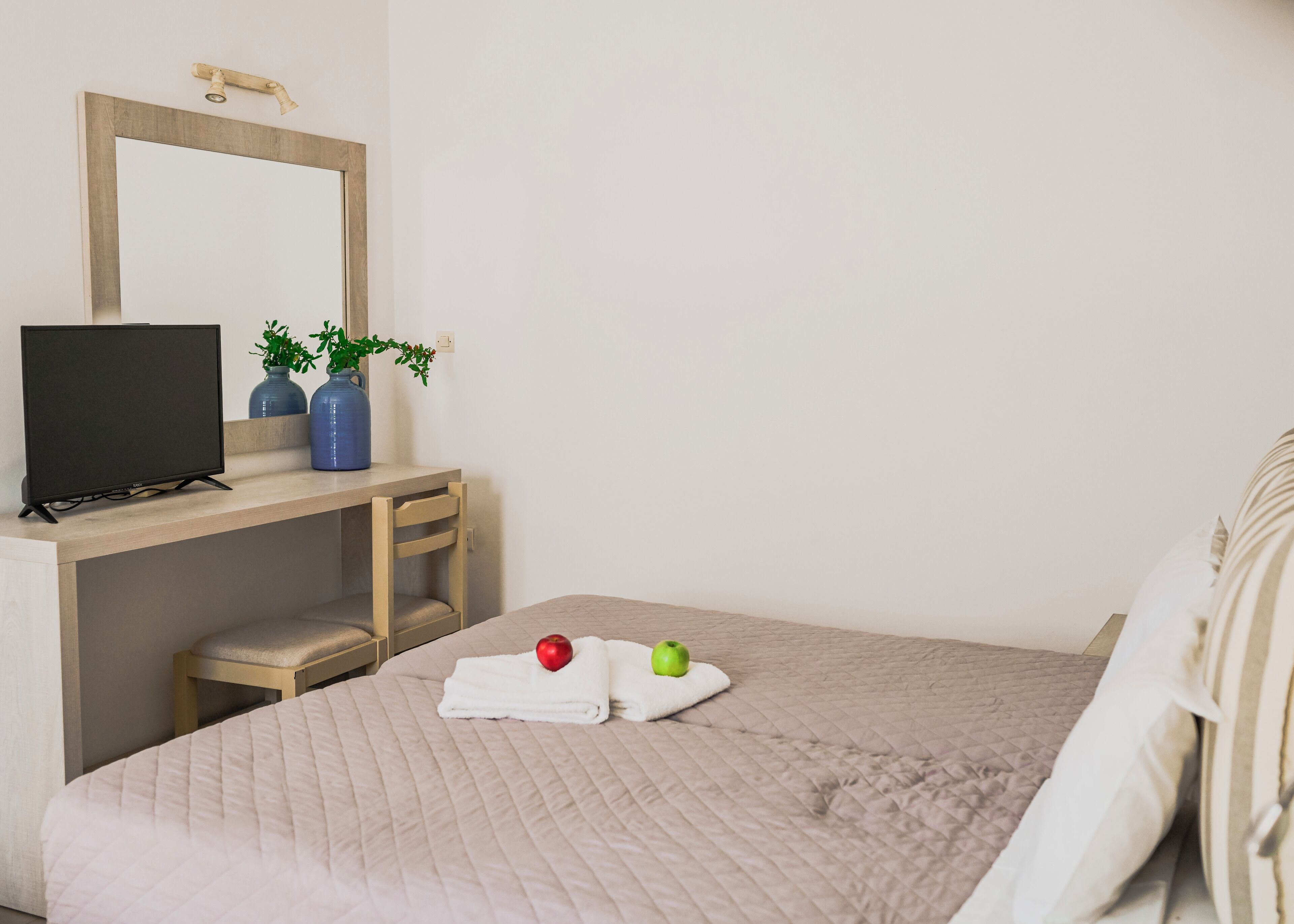 Ein Hotelzimmer mit einem Bett, einem Schreibtisch mit Computer, einem Sessel, einem Spiegel und zwei Vasen mit Pflanzen.