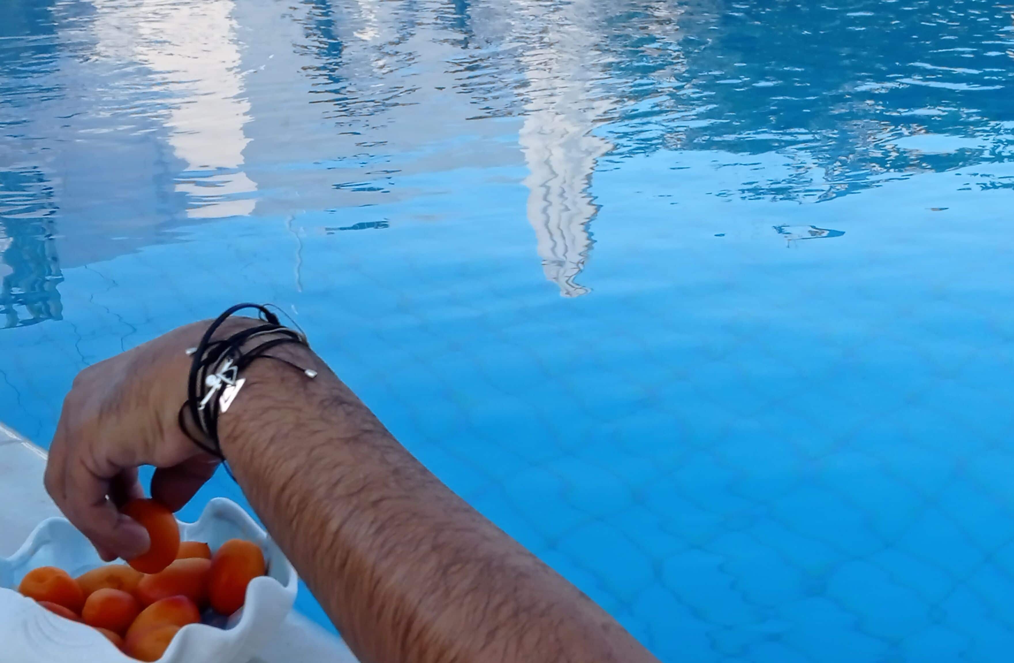 Une main plongeant dans un bol de collations près d’une piscine.