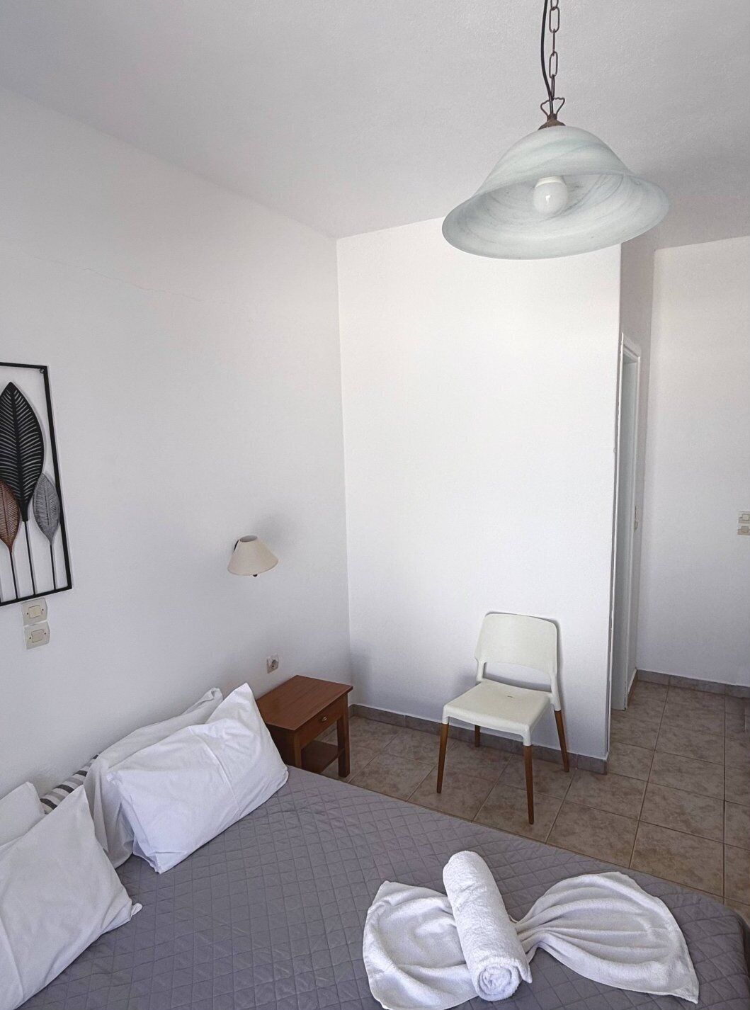 Une chambre d’hôtel avec un lit, une chaise, une petite table, une lampe et un luminaire au plafond.