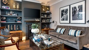 A modern living room with a grey sofa, a coffee table, and a fireplace. There are shelves with decorative items and a flat-screen TV mounted on the wall. - Luxurious Wandsworth Home Close to Putney Heath by Underthedoormat (London)