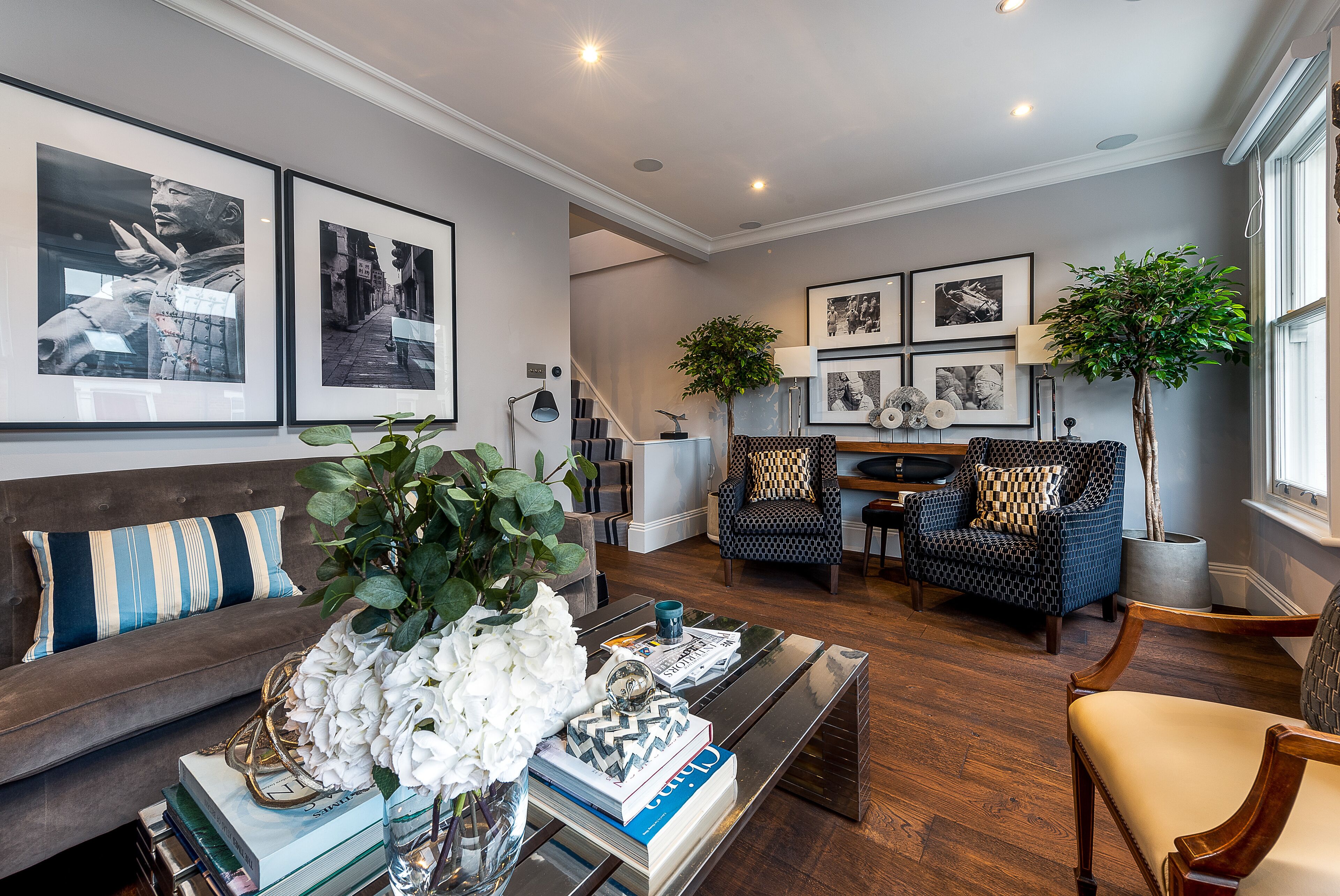 A modern living room with a sofa, armchair, and coffee table, featuring artwork and a potted plant.