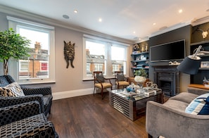 A living room with a fireplace, two armchairs, a sofa, a coffee table, and a TV. - Luxurious Wandsworth Home Close to Putney Heath by Underthedoormat (London)
