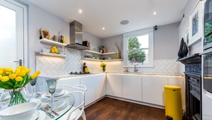 A modern kitchen with white cabinets, a herringbone tile backsplash, and a yellow trash bin. - Luxurious Wandsworth Home Close to Putney Heath by Underthedoormat (London)