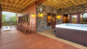 Une terrasse en bois avec des fauteuils à bascule, un jacuzzi et des murs en pierre.