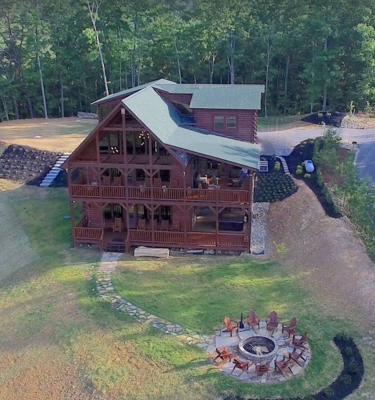 A two-story log cabin with a balcony, a stone fire pit, and a stone staircase leading to the entrance.