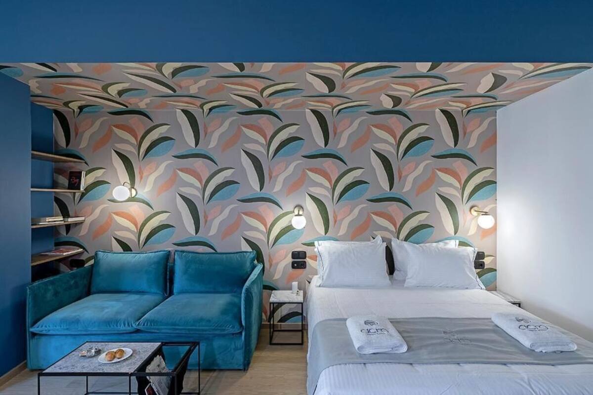 A hotel room with a sofa, a bed, a nightstand, and a wall with a leaf pattern.