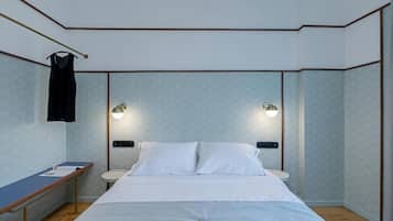 A modern hotel room with a bed, bedside tables, and wall-mounted lights.