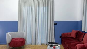 A room with a blue and white wall, a grey curtain, a red sofa, a grey armchair, and a small table with a camera and an apple.
