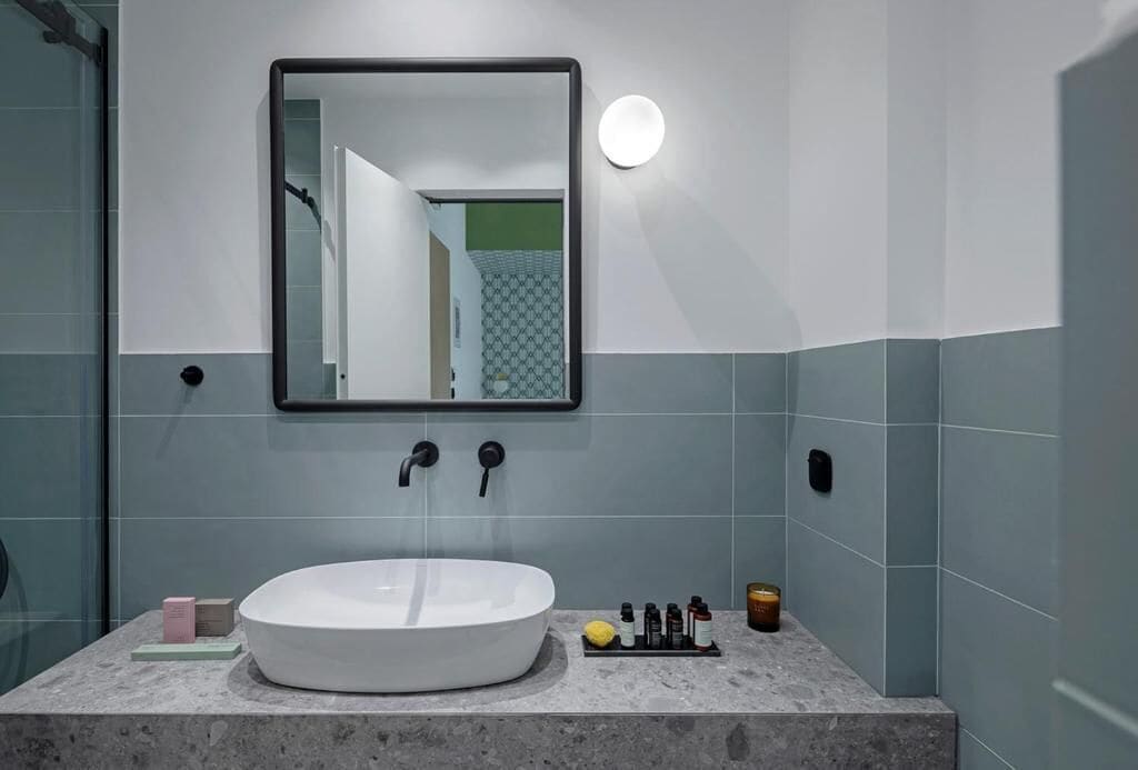 A bathroom with a round white sink, a mirror, and a wall-mounted light.