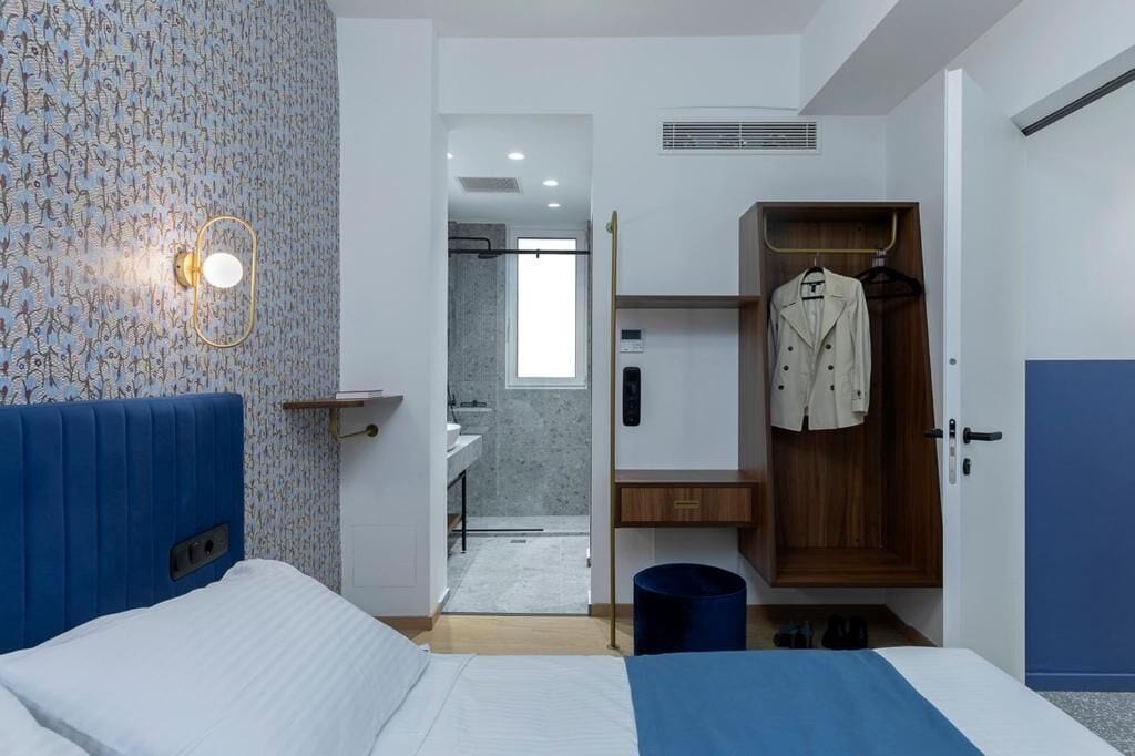 A modern hotel room with a bed, a wardrobe, a bathroom, and a shower area.
