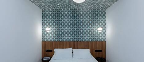 A hotel room with a patterned ceiling, a bed with white linens, and a wooden headboard.