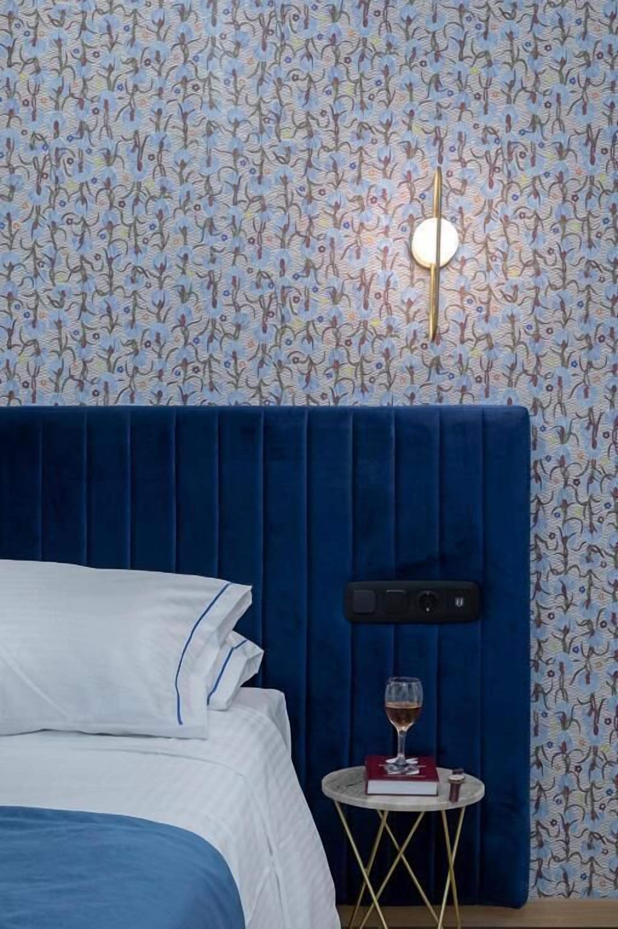 A bedroom with a blue headboard, a white bedspread, and a small bedside table with a book and a glass of wine.