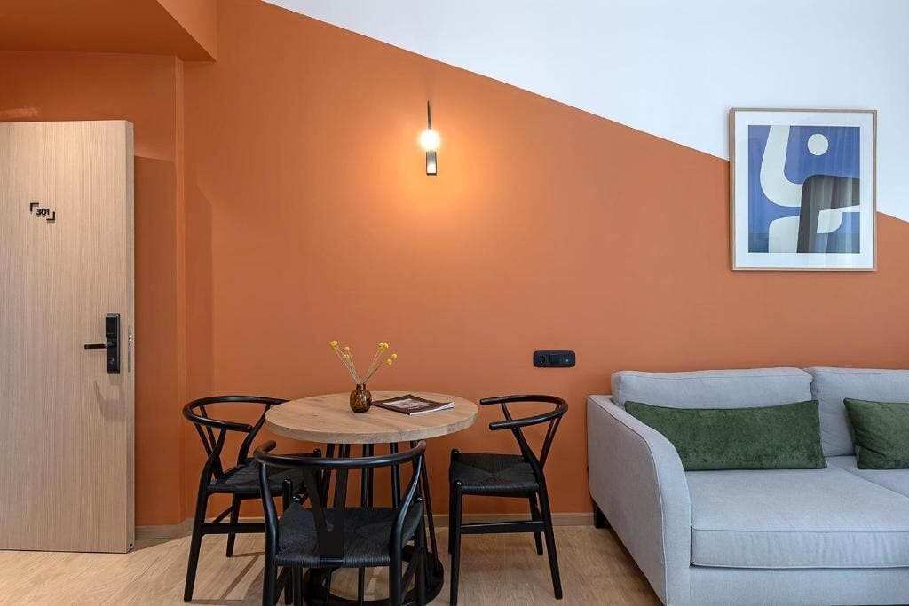 A modern living room with a round table, four chairs, a sofa, and a painting on the wall.