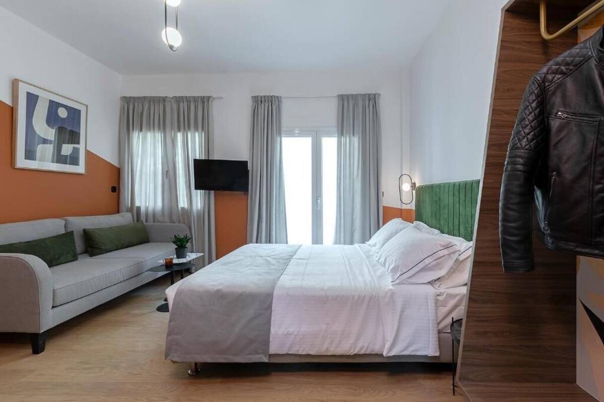 A modern hotel room with a bed, a sofa, a TV, and a coat rack.