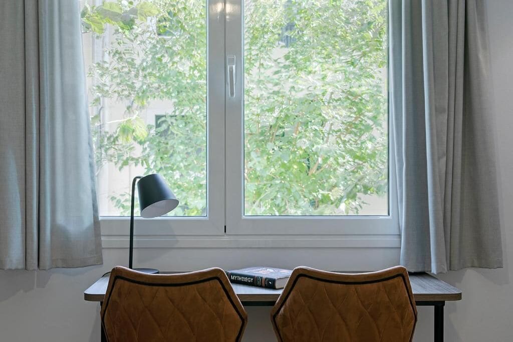 Una habitación con escritorio, dos sillas, lámpara y ventana con cortinas.