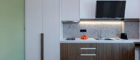 A modern kitchen with a built-in oven, a microwave, a sink, and a flat-screen TV mounted above the countertop.