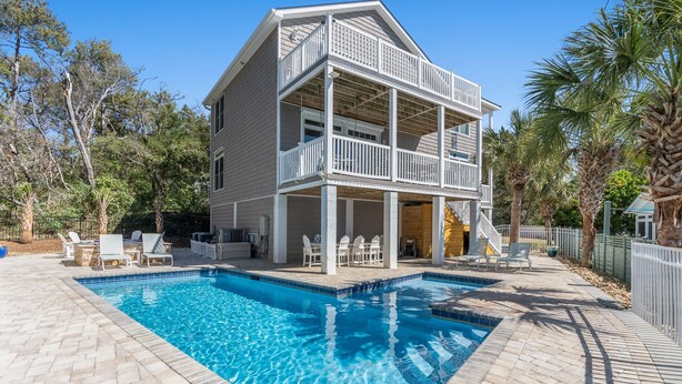 A two-story house with a swimming pool, outdoor furniture, and a fenced yard.