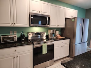 A kitchen with white cabinets, a stainless steel microwave, a toaster, a coffee maker, and a refrigerator.