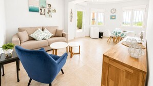 A bright living room with a sofa, a blue chair, a small table, and a dining area with a wooden table and chairs. - Beautifull villa with sea views in La Florida (Denia)