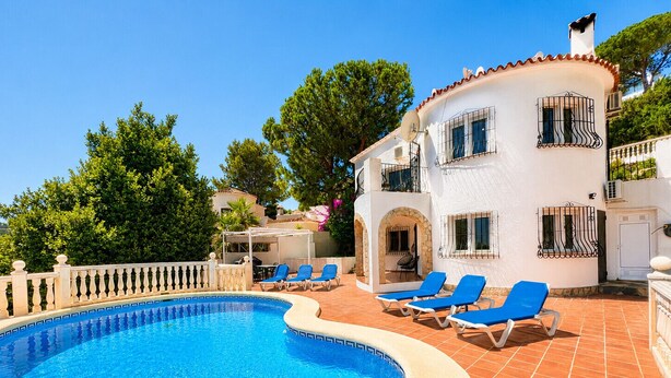 A swimming pool with lounge chairs, a white building with balconies, and a stone wall. - Beautifull villa with sea views in La Florida (Denia)