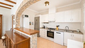 A kitchen with white cabinets, a stone arch, a wooden bar, and a stainless steel refrigerator. - Beautifull villa with sea views in La Florida 4 p. (Denia)