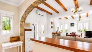 A kitchen with a stone arch, wooden ceiling beams, a white refrigerator, a dining area with a sofa and table, and a TV. - Beautifull villa with sea views in La Florida 4 p. (Denia)