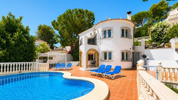 A pool area with a curved pool, blue lounge chairs, and a white building with balconies. - Beautifull villa with sea views in La Florida 4 p. (Denia)