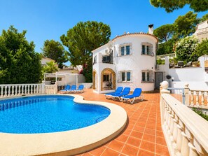 A pool area with a curved pool, blue lounge chairs, and a white building with balconies. - Beautifull villa with sea views in La Florida 4 p. (Denia)