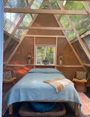 A cozy, triangular attic bedroom with a bed, two nightstands, a window, and a view of trees. - Private Lakeside A-Frame Tent (Ellsworth)