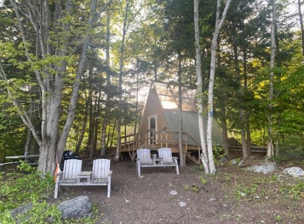 A cabin with a wooden deck and two Adirondack chairs in a forest setting. - Private Lakeside A-Frame Tent (Ellsworth)
