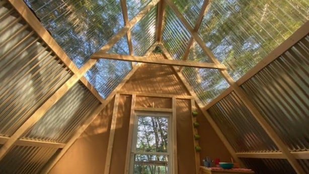 Un dormitorio en el ático con forma triangular, un tragaluz, una cama y un pequeño aparador.