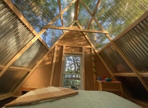 A triangular attic bedroom with a skylight, a bed, and a small dresser. - Private Lakeside A-Frame Tent (Ellsworth)