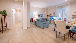 Ein modernes Wohnzimmer mit einem blauen Sofa, einem Esstisch mit Stühlen und einer Küchenzeile im Hintergrund.