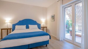 Ein Schlafzimmer mit einem Bett, zwei Nachttischen, einem Fenster mit Blick ins Freie und einer Tür zu einem Balkon.