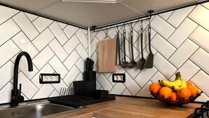 Cozinha com painel de azulejos em padrão herringbone, torneira preta, armário de madeira e uma fruteira no balcão.