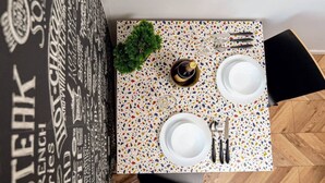 Uma mesa de jantar com superfície em terrazzo, duas pratos brancos, uma garrafa de vinho e talheres.
