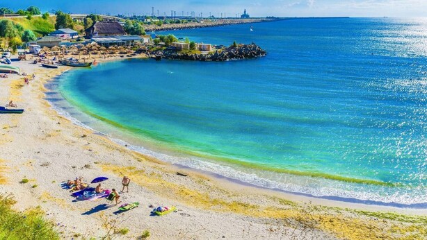 Uma praia com águas turquesa cristalinas, areal dourado e algumas pessoas relaxando.
