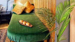 Um quarto aconchegante com uma cama verde, venezianas de madeira, uma escrivaninha e um vaso com planta.