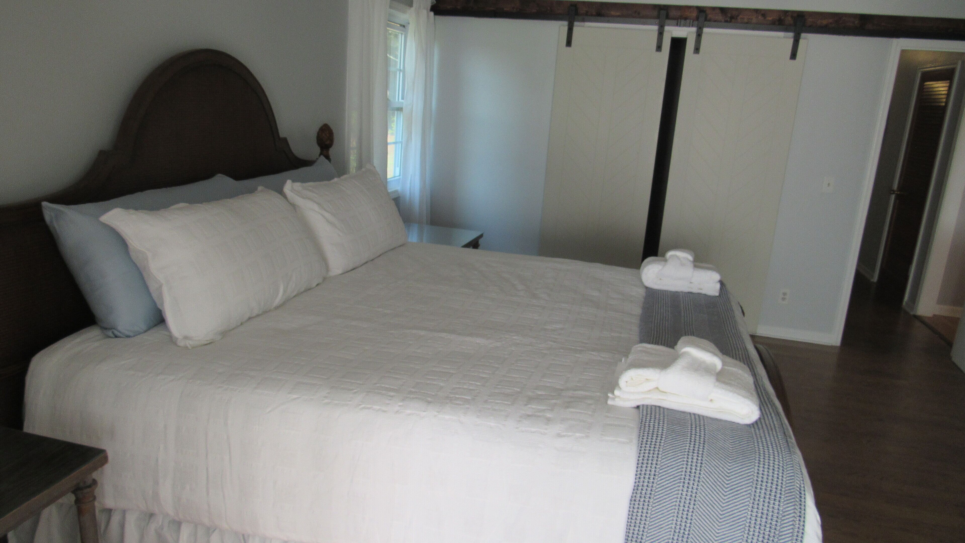 A neatly made bed with a wooden headboard, a bedside table, and a window with curtains.
