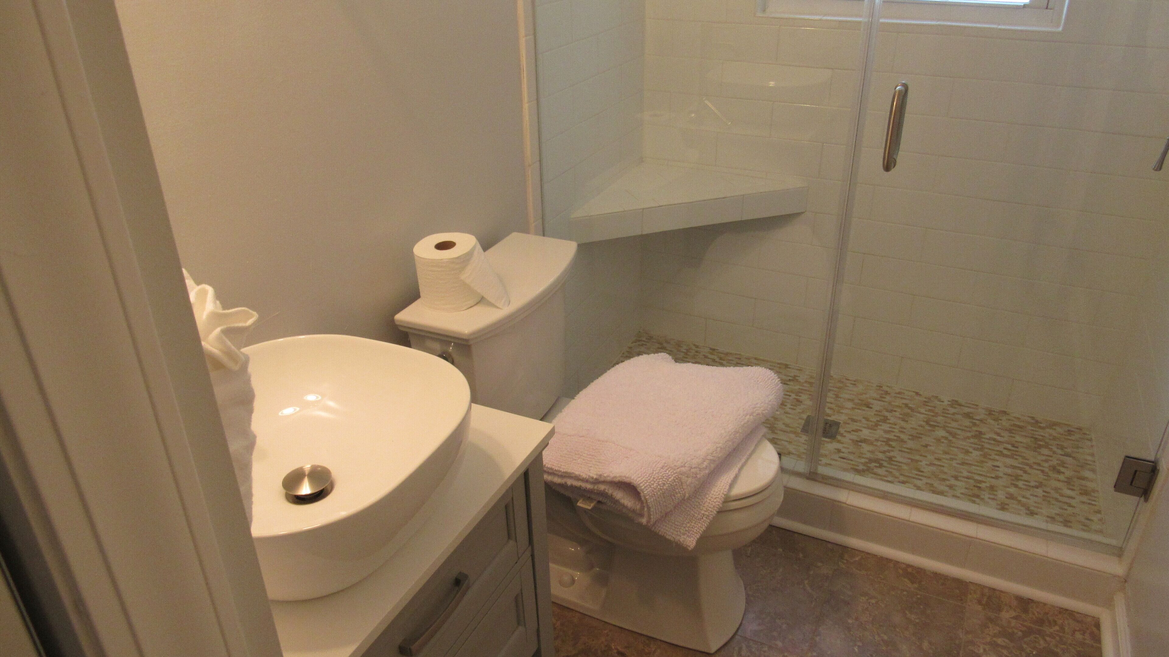 A bathroom with a white sink, toilet, and a glass shower enclosure.