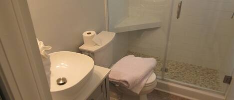 A bathroom with a white sink, toilet, and a glass shower enclosure.
