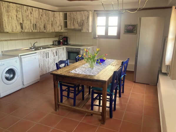 A compact kitchen with a wooden table, blue chairs, a washing machine, and a refrigerator.