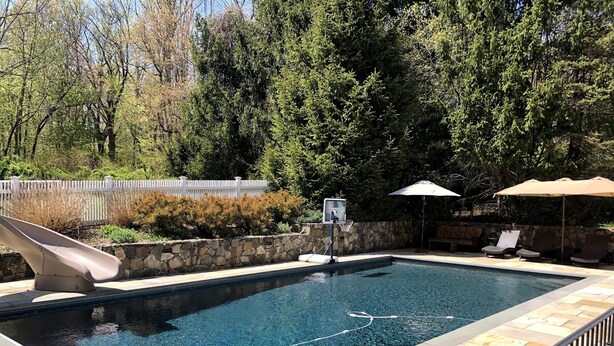 A swimming pool with a slide, surrounded by a stone wall and a white fence. - Country Living with Heated Pool and Hot Tub (Bedford)
